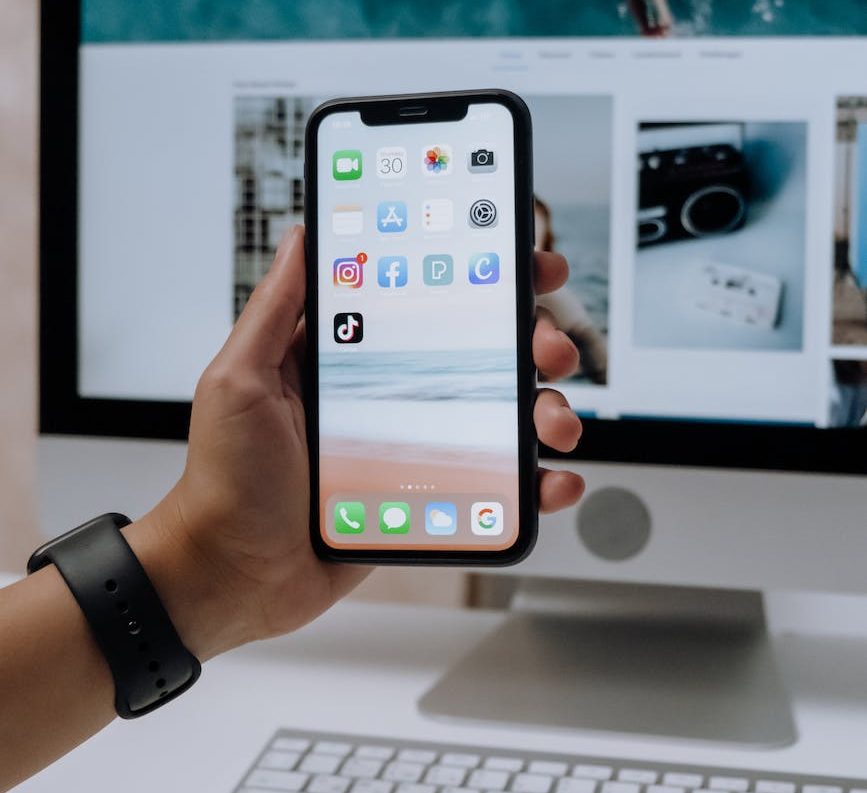 holding a smartphone in front of an imac