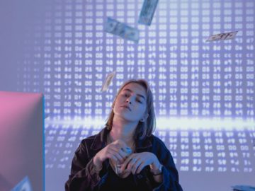 A woman sitting at a desk with money falling from the ceiling.