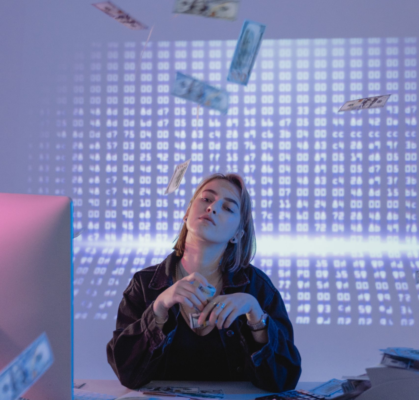 A woman sitting at a desk with money falling from the ceiling.